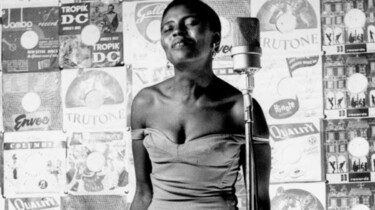 Szenenbild: Miriam Makeba am Mikrofon vor Plakatwand