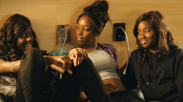Szenenbild: drei der Mädchen sitzen vor einer Wand in einem Hotelzimmer und quatschen