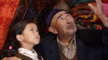 Szenenbild: Enkelin und Großvater mit Tüchern im Hintergrund, sie schauen nach rechts oben