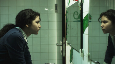 Szenenbild: Charo in der Schultoilette, sie schaut sich im Spiegel an und ist von der Seite zu sehen