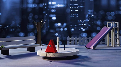 Filmstill Edgy, ein rotes Dreieck sitzt auf einem Drehgefährt auf einem Spielplatz