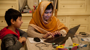 Szenenbild: Malala mit ihrem kleinen Bruder am Küchentisch am Laptop