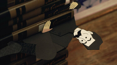 Szenenbild: eine Papierfigur schaut aus einem Stapel Bücher hervor