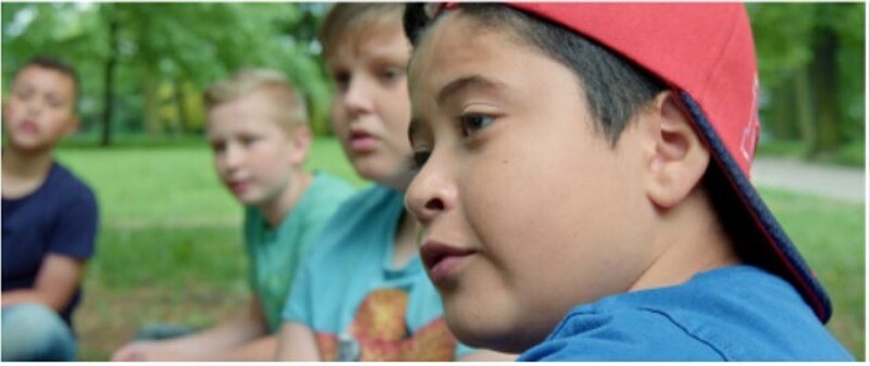 Filmstill "Wie ein Wald", ein paar Kinder sitzen auf einer Wiese, ein Junge im Halbprofil