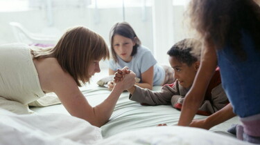 Szenenbild: Kinder auf einem Bett machen Armdrücken
